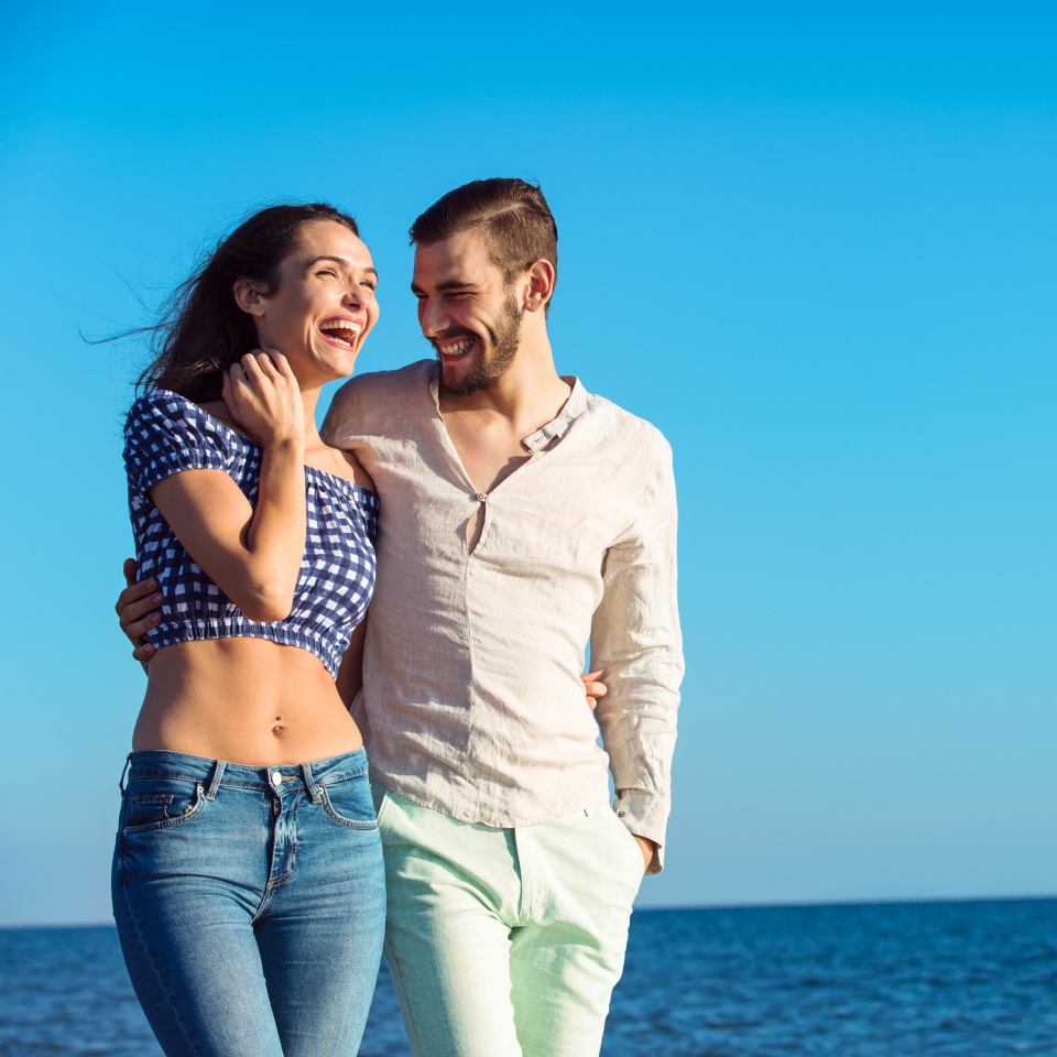 Couple walking on beach. Young happy interracial couple walking on beach smiling holding around each other. Latino woman, Caucasian man.