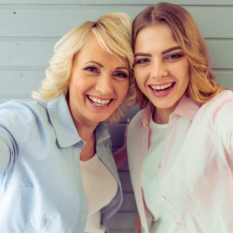 Retrato de una hermosa madre madura y su hija abrazándose mirando a la cámara y sonriendo sobre un fondo gris