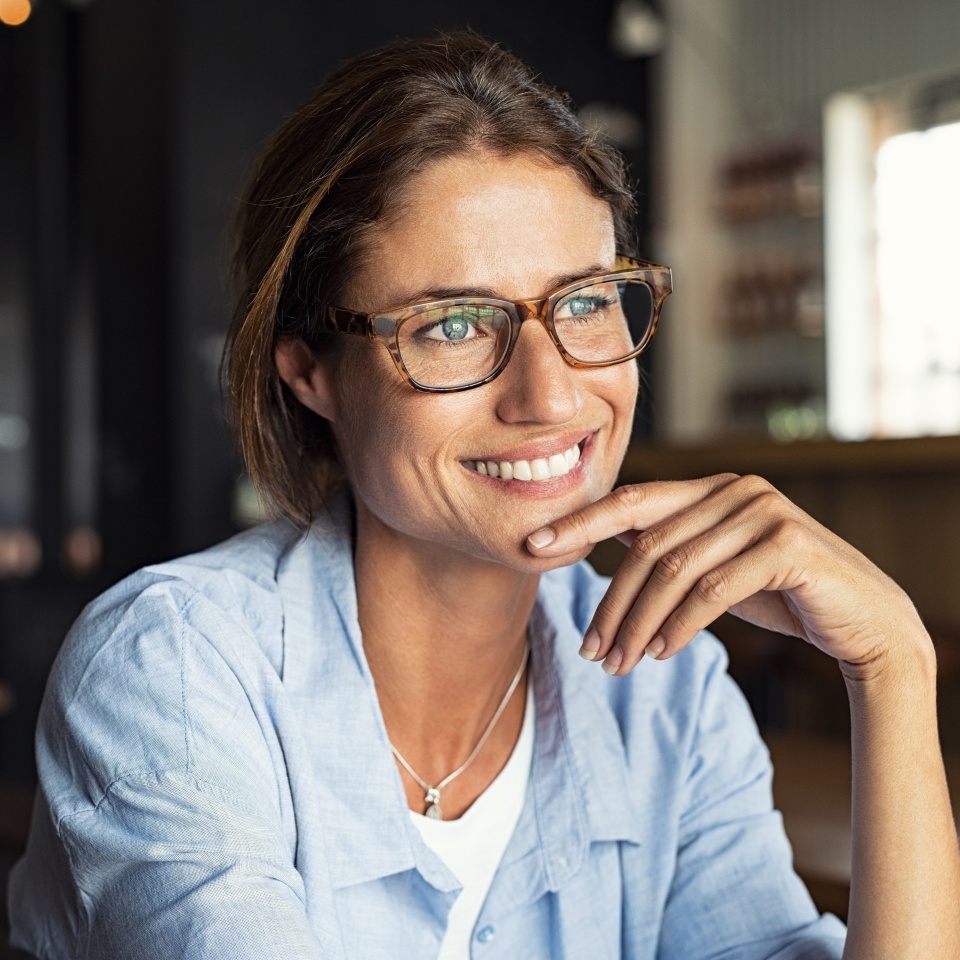 Retrato de una hermosa mujer madura sentada en una cafetería mirando hacia otro lado. Alegre mujer madura con gafas pensando con el dedo en la barbilla. Mujer feliz relajándose en una cafetería y sonriendo.  