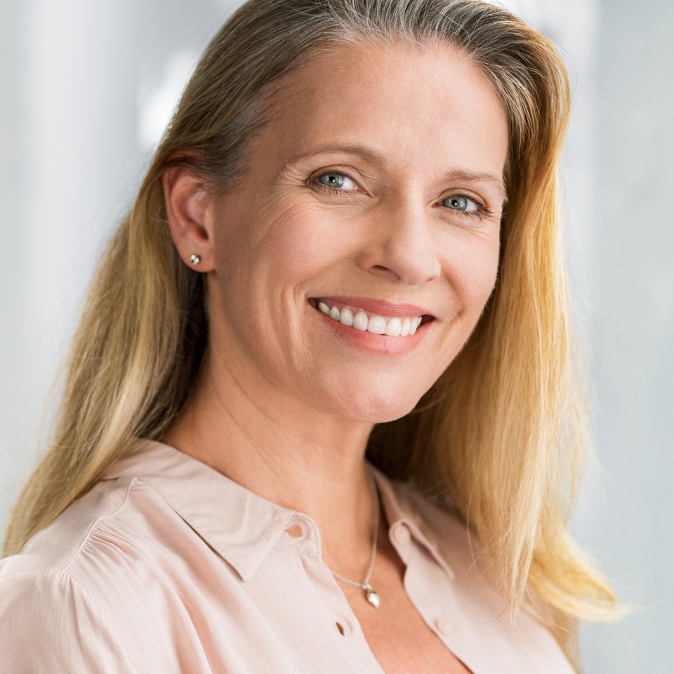 Portrait of mature woman enjoying life after retirement and looking at camera. Closeup face of happy senior woman with blond hair smiling. Beautiful smiling lady indoor.