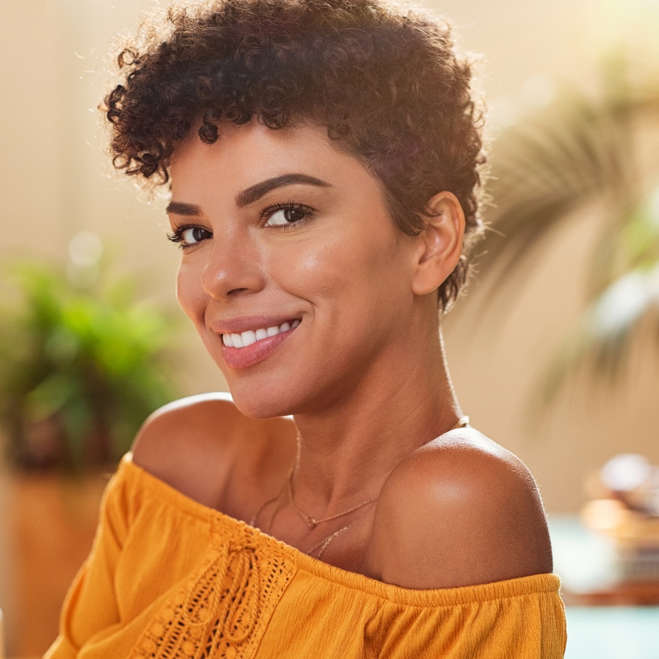 Portrait of natural beautiful girl smiling and looking at camera. Closeup face of brazilian young woman with curly hair. Charming african woman sitting at cafeteria.
