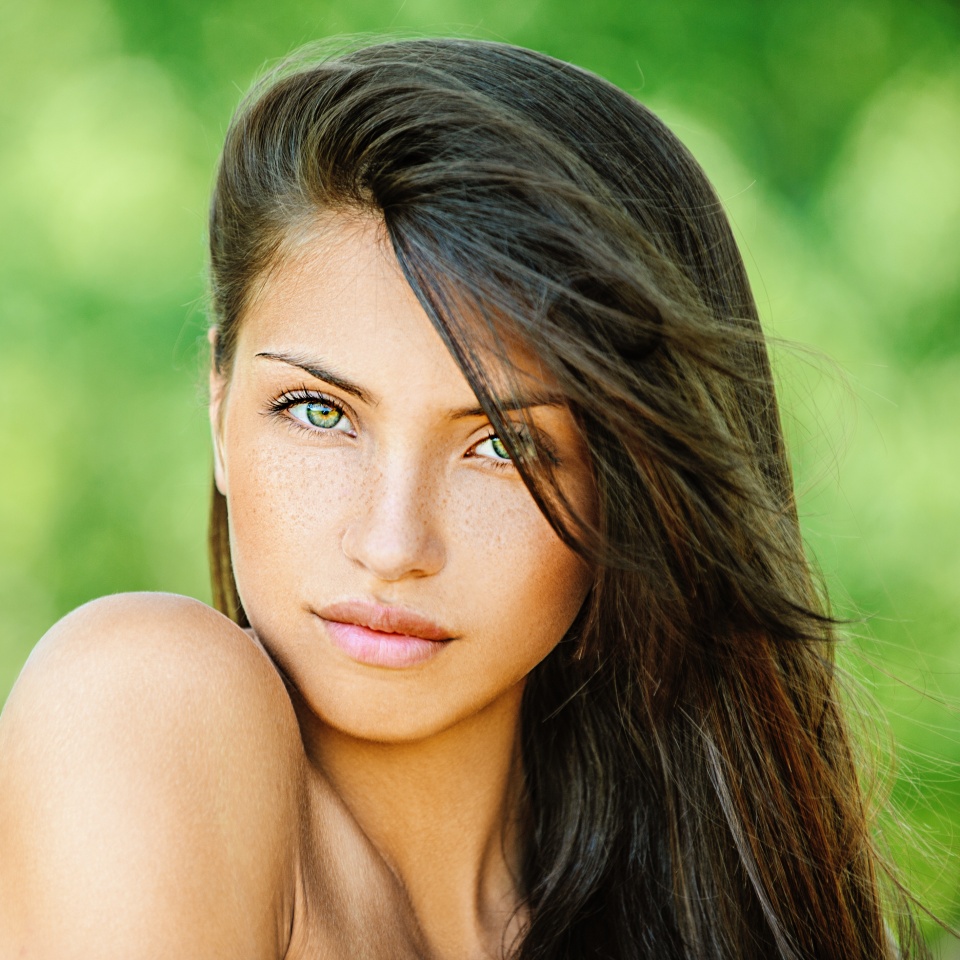 Retrato de una joven y bella mujer con los hombros descubiertos, sobre un fondo verde de naturaleza veraniega.