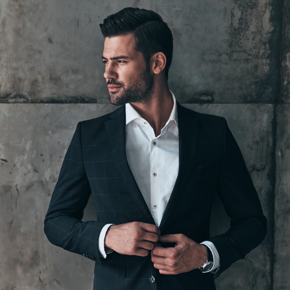 Charming man. Handsome young man in suit looking away and adjusting his jacket while standing indoors