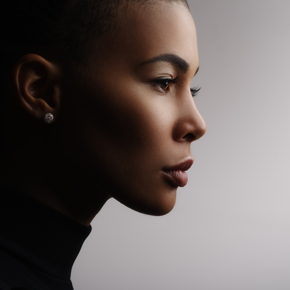 Primer plano de un retrato de moda de una joven mestiza con una piel perfecta, lisa y brillante, labios carnosos, cabello recogido y cuello largo. Foto de estudio del rostro de una modelo afroamericana, de perfil 