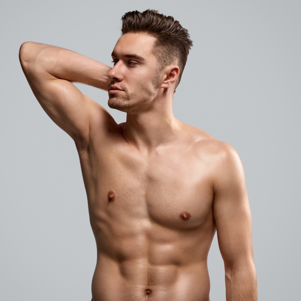 Strong shirtless bodybuilder with hand behind head looking away against gray background