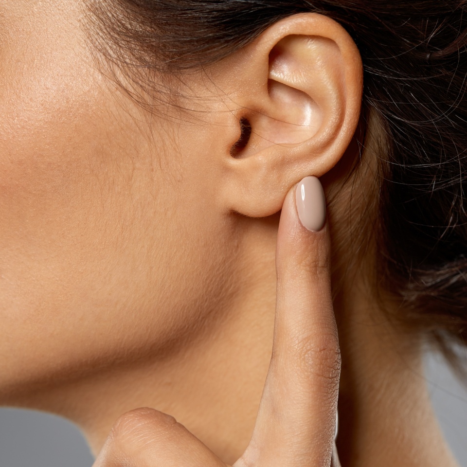 hearing, people and beauty concept - close up of young woman pointing finger to her ear over grey background