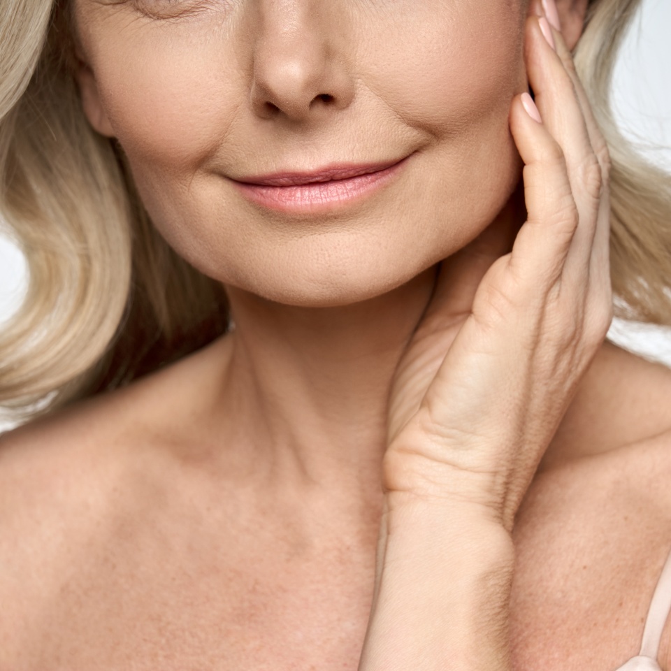 Face close up portrait of happy mid age 50 years old woman touching face with hand. Advertising of skin care anti wrinkle products for facial bottom part, lips, chin neck and decollete.