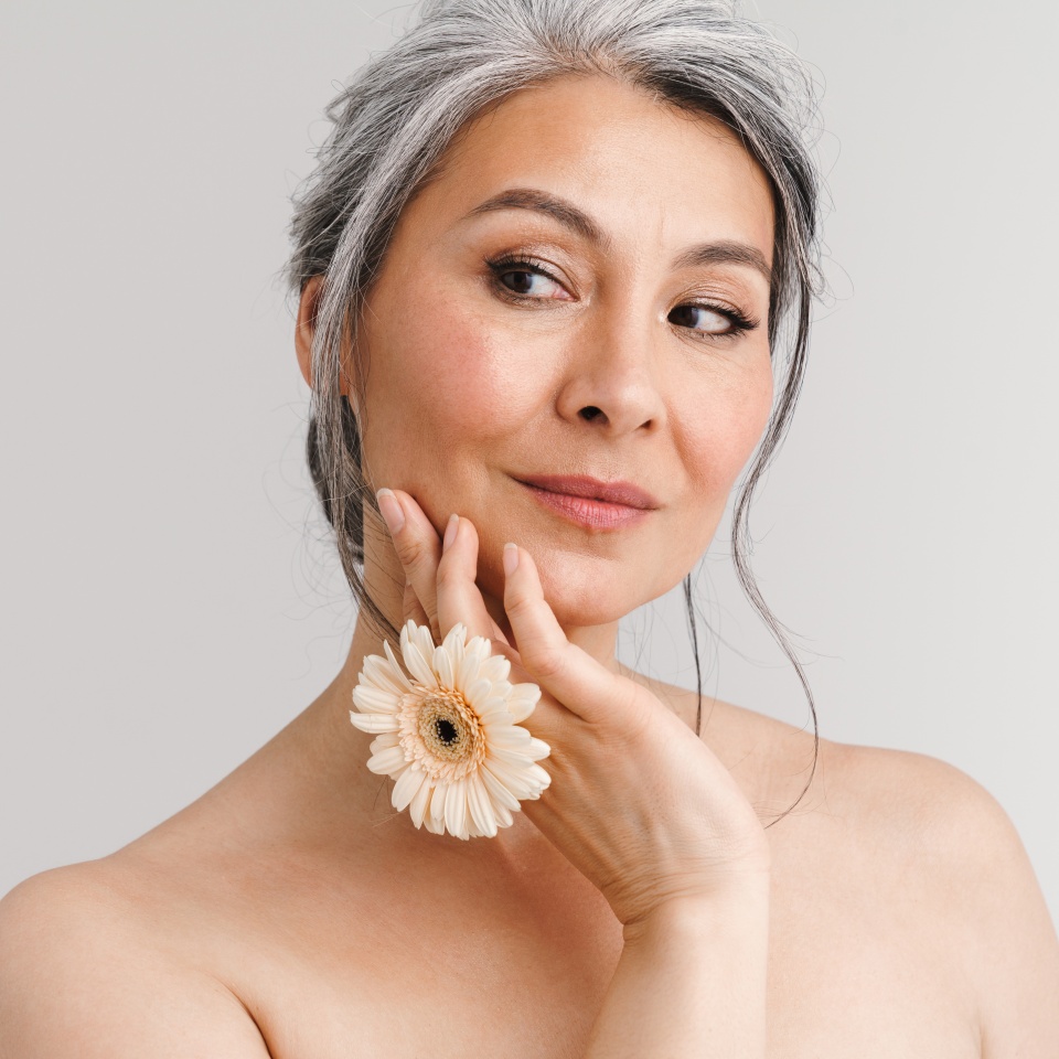 Shirtless woman with grey hair looking aside while posing with gerbera isolated over white background
