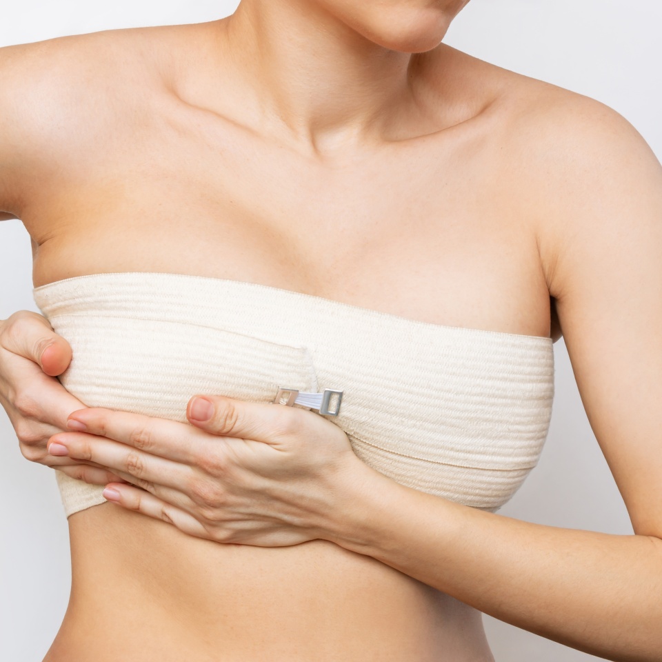 Cropped shot of young woman with elastic bandage after breast augmentation with silicone implants isolated on white background.The result of lifting. Breast size correction. Pain after plastic surgery