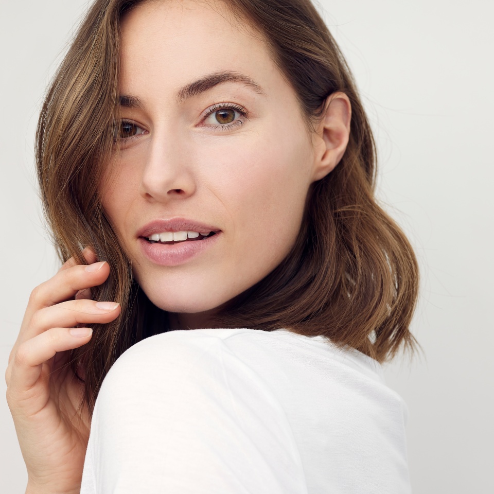Retrato de una hermosa mujer morena natural, sonriendo y mirando sexy a la cámara. Primer plano de una linda chica aislada sobre fondo blanco. 