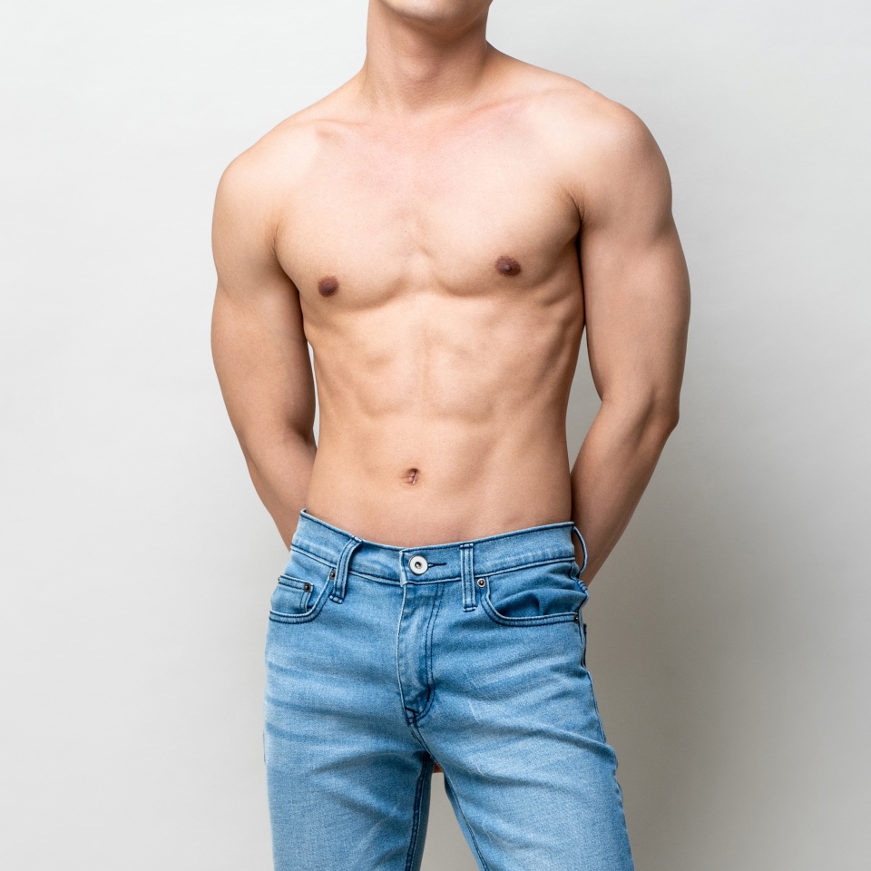 Shirtless muscular male model body on gray isolated background in light studio