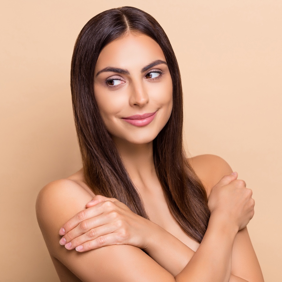 Portrait of attractive long-haired girl hugging shoulders looking aside copy space isolated over beige pastel color background