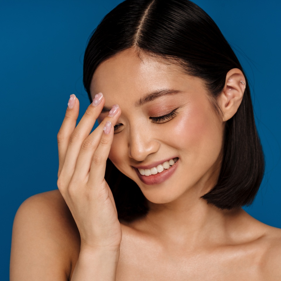 Young beautiful smiling happy asian woman with closed eyes touching her nose bridge, while standing over isolated blue background