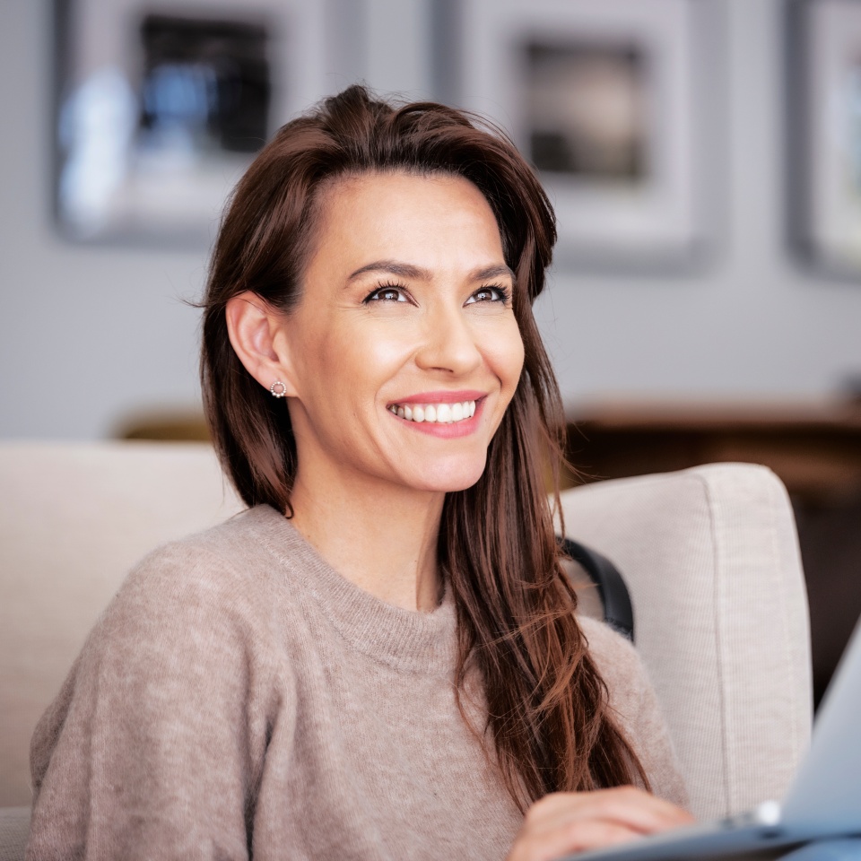 Close-up of an attractive middle aged woman sitting on armchair while using laptop. Beautiful female wearing casual clothes. Home office.