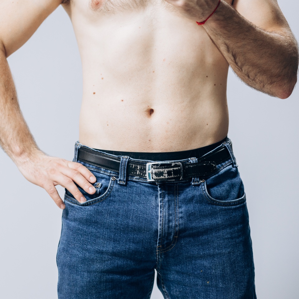 A man with a naked torso in his pants. Buttocks of a man in blue jeans. Problems with the urethra. hemorrhoids