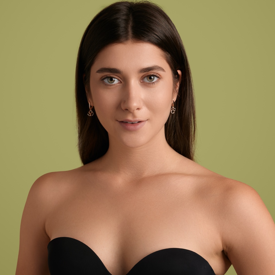 Beautiful young female in black lingerie looking at camera with smile on green background in studio with copy space