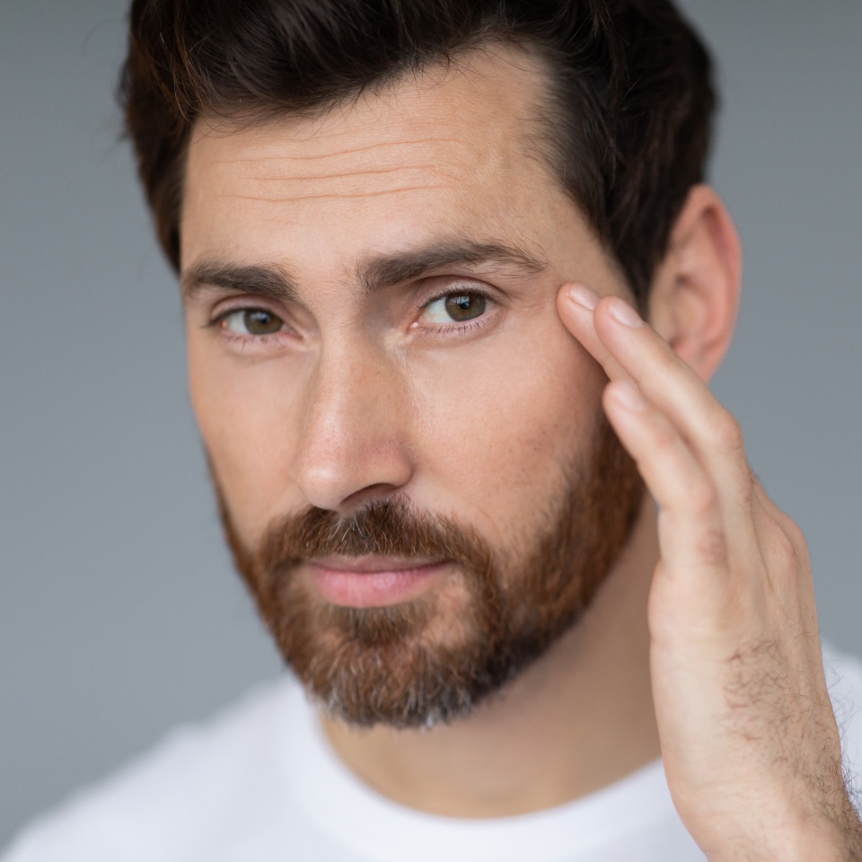 Anti-aging eye care treatment. Handsome middle aged man touching under eyes skin and looking at camera, closeup, grey studio background, copy space