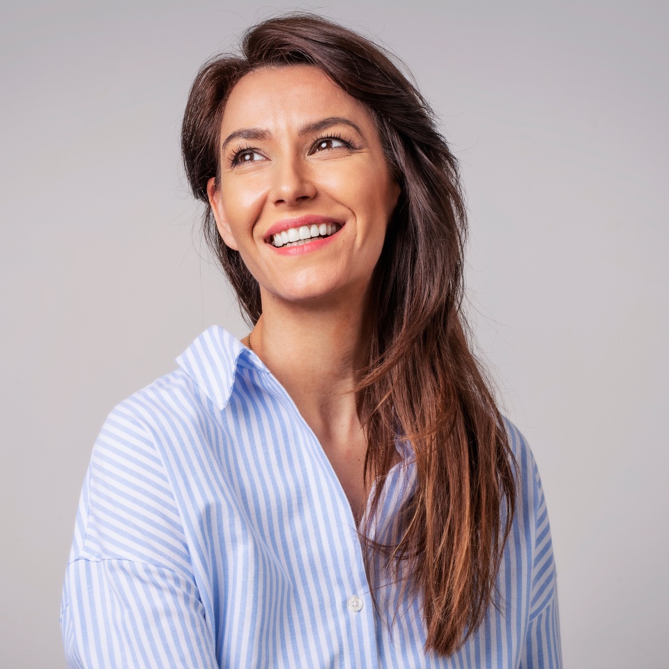 Smiling brunette businesswoman sitting against gray background. Confident female professional is wearing blue shirt. She is having brown hair. Copy space.