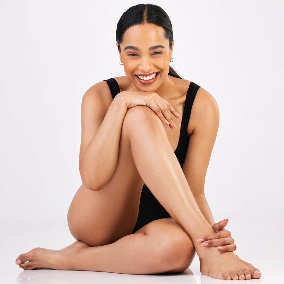 Woman, underwear and healthy body in studio portrait with smile, sitting and happiness by white background. Girl, model and young with beauty, lingerie and glow on skin with excited face on floor