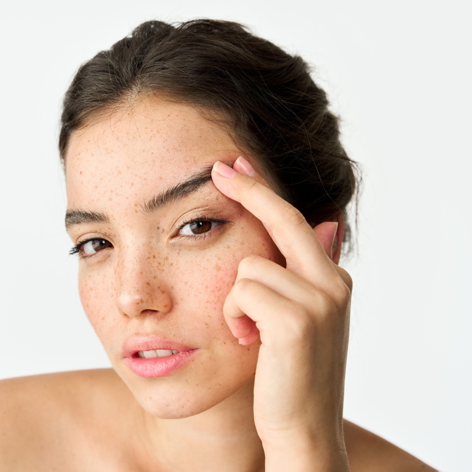 Mujer latina joven adulta, chica morena genial de la generación Z con pecas en la cara mirando a la cámara levantando la ceja aislada sobre fondo blanco. Retrato de estética de belleza. Cuidado de la piel, cirugía ocular y anuncio cosmético  