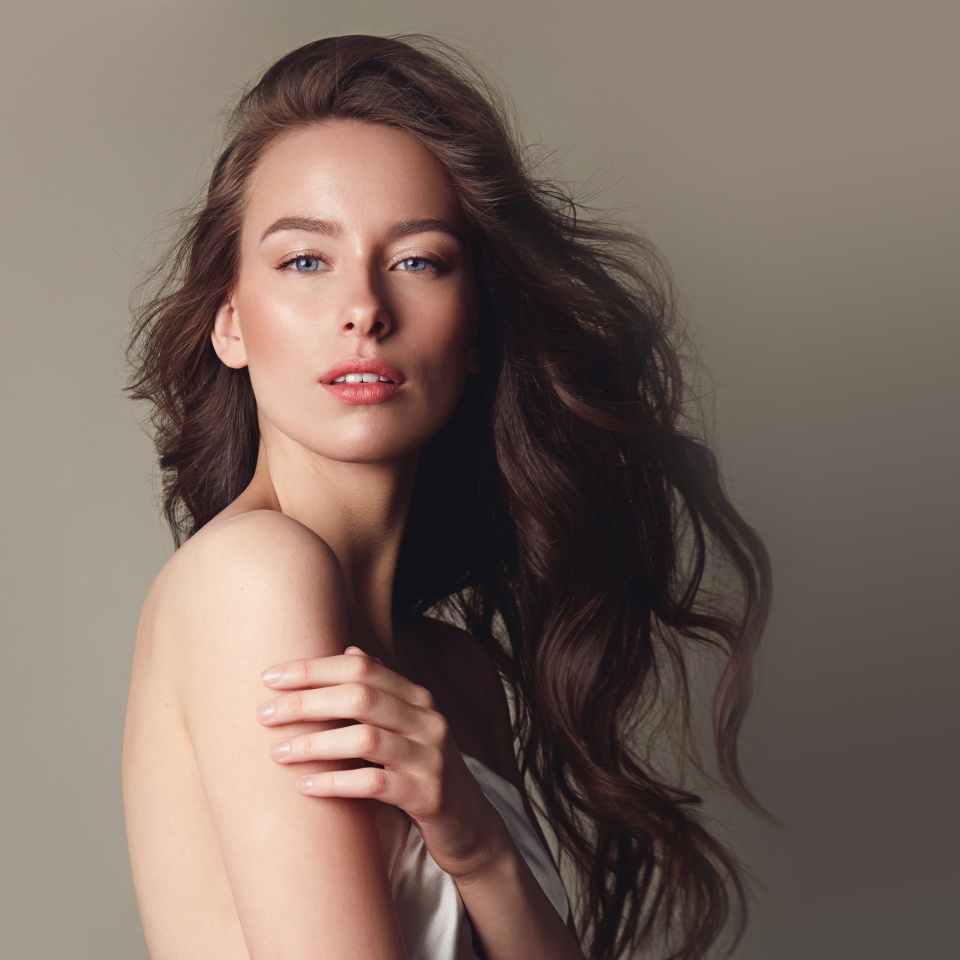 A beautiful young girl with long curly hair poses in the studio in different poses on a beige background. Natural care cosmetics, natural beauty. Advertising of natural hair cosmetics.