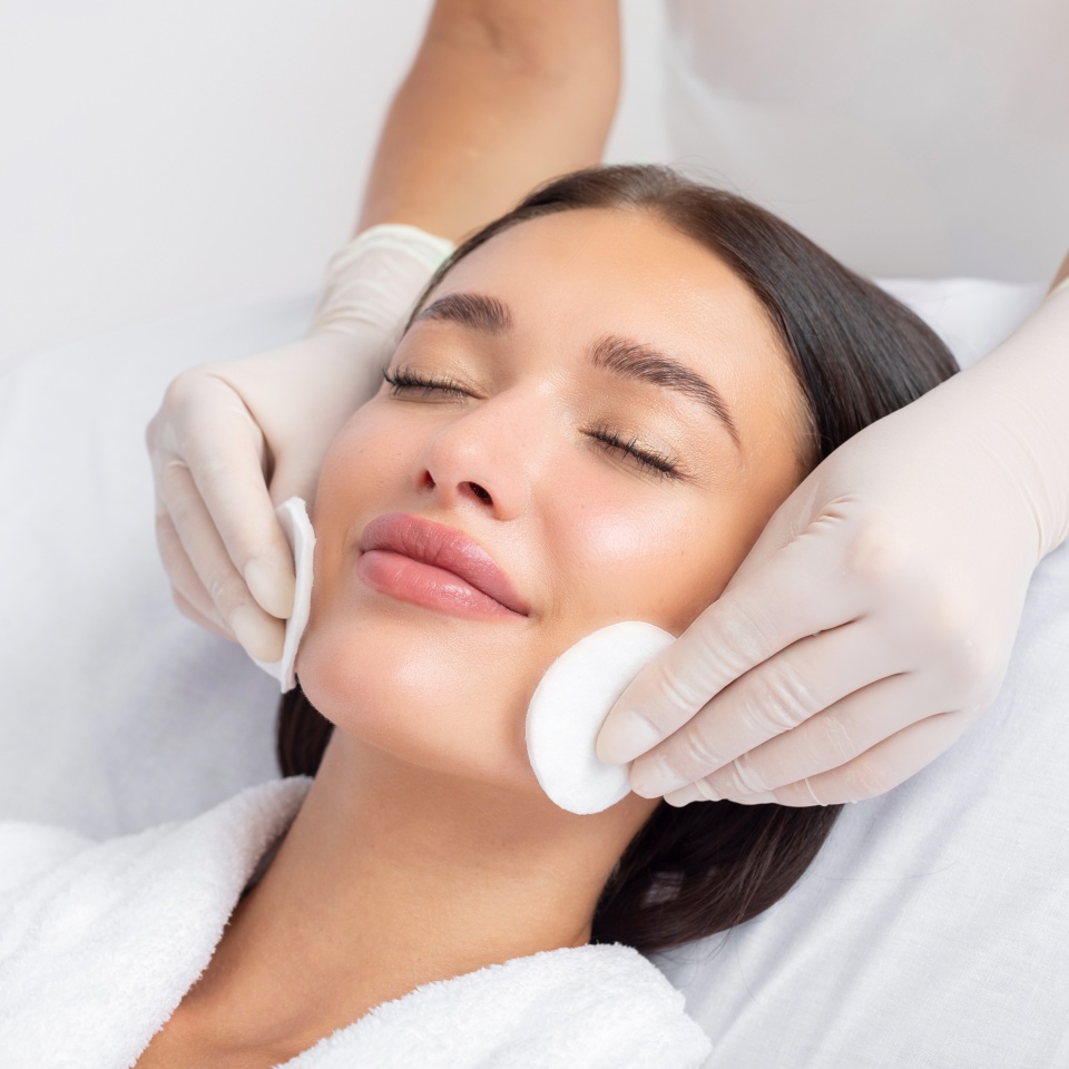 Female beautician cleansing skin of young woman, cosmetology procedure in beauty salon. Anti-age procedures at spa clinic