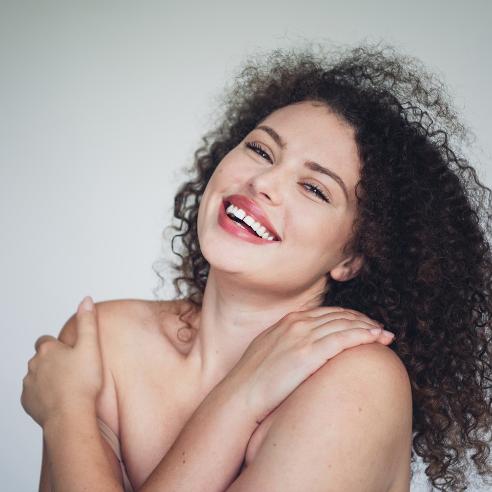 Confident young woman embracing natural beauty with an unretouched portrait showcasing curly hair and a positive smile