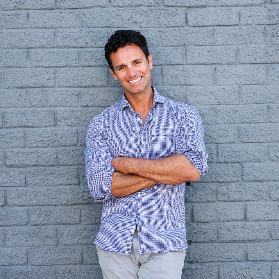 Portrait of a handsome older man smiling with arms crossed against gray background