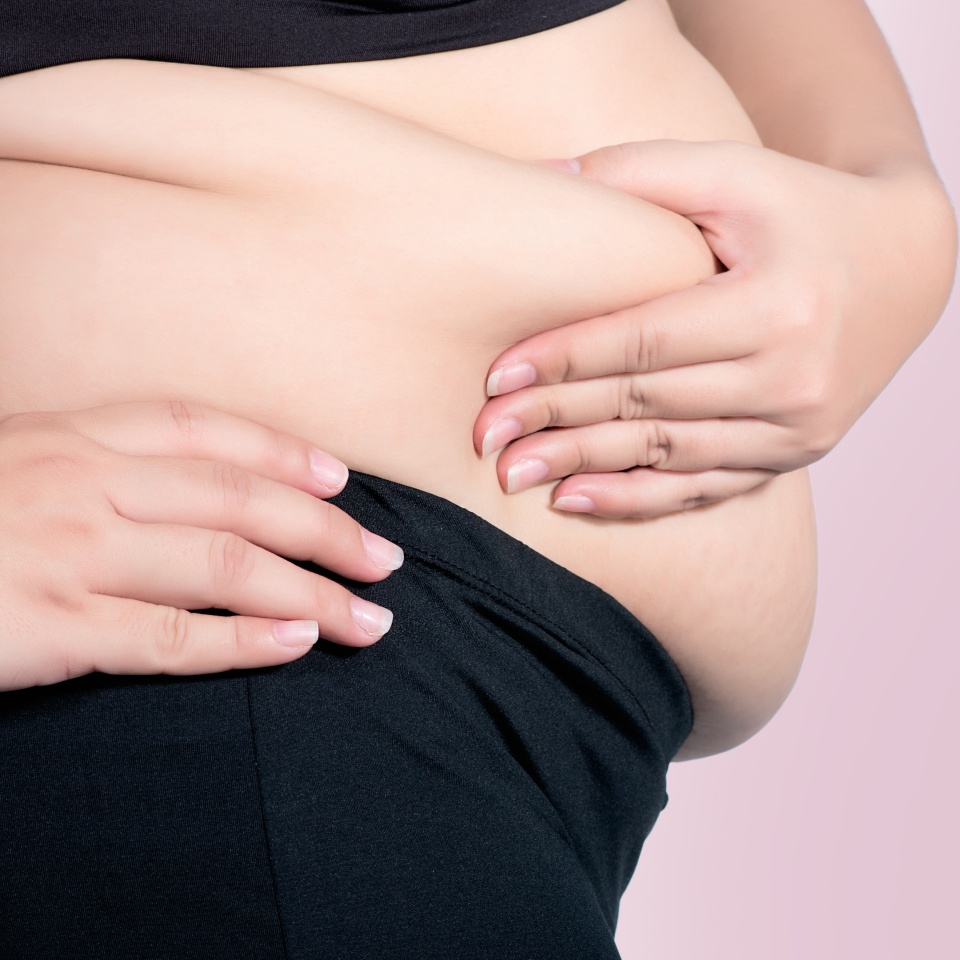 Close-up of a person’s midsection, showing hands holding their stomach and the waistband of black pants against a plain background.