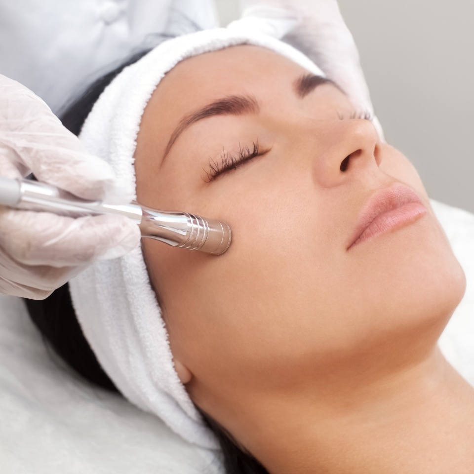 The cosmetologist makes the procedure Microdermabrasion of the facial skin of a beautiful, young woman in a beauty salon.Cosmetology and professional skin care.