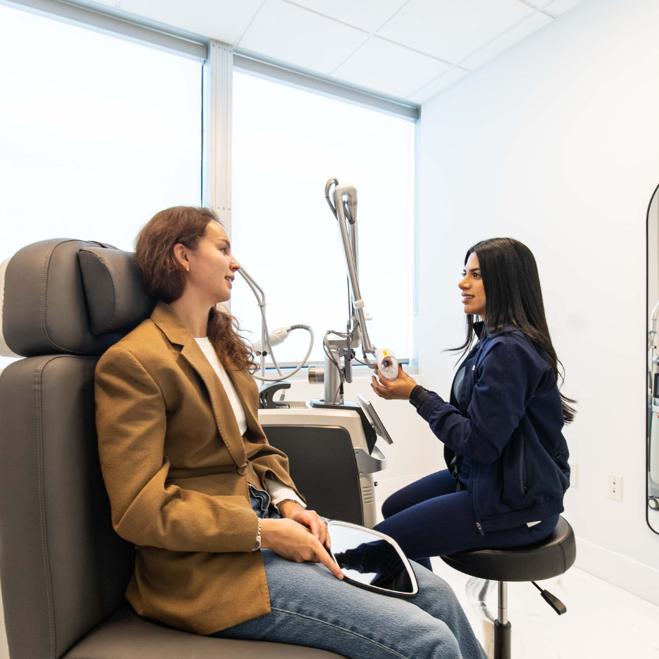 A healthcare professional talks to a seated patient in a modern medical office, holding a device and explaining its use.